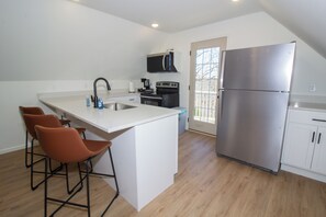 Una cocina con una isla central, taburetes de bar, microondas, estufa y refrigerador.