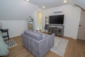 A living room with a grey sofa, a flat-screen TV, a wooden entertainment unit, and a patterned rug.