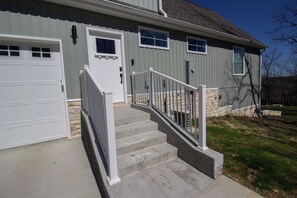 A residential house with a front garage, a set of concrete steps leading to a white door, and a stone foundation.