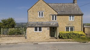 A two-story stone house with a gabled roof, a front door, and a small porch. - Murray's Cottage -  a cottage that sleeps 5 guests  in 3 bedrooms (Clapton-on-the-Hill)