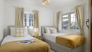 A hotel room with two beds, a bedside table with a lamp, and a window with curtains. - Murray's Cottage -  a cottage that sleeps 5 guests  in 3 bedrooms (Clapton-on-the-Hill)