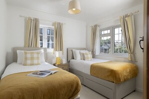 A hotel room with two beds, a bedside table with a lamp, and a window with curtains. - Murray's Cottage -  a cottage that sleeps 5 guests  in 3 bedrooms (Clapton-on-the-Hill)
