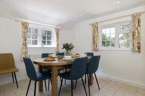 A dining area with a round wooden table, six chairs, and a vase of flowers. - Murray's Cottage -  a cottage that sleeps 5 guests  in 3 bedrooms (Clapton-on-the-Hill)