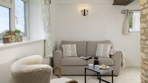 A cozy living room with a sofa, a chair, a coffee table, and a window with curtains. - Murray's Cottage -  a cottage that sleeps 5 guests  in 3 bedrooms (Clapton-on-the-Hill)