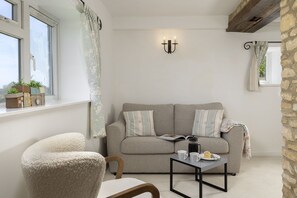 A cozy living room with a sofa, a chair, a coffee table, and a window with curtains. - Murray's Cottage -  a cottage that sleeps 5 guests  in 3 bedrooms (Clapton-on-the-Hill)