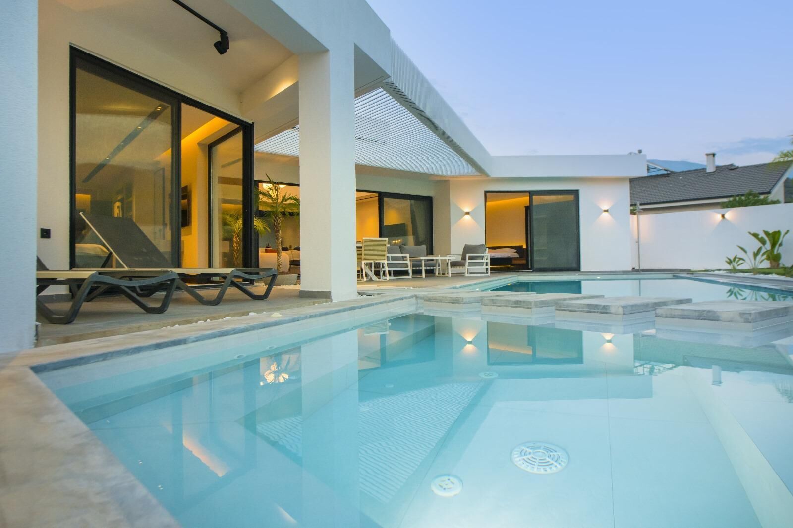 A modern outdoor swimming pool with lounge chairs and a covered seating area.
