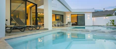 A modern outdoor swimming pool with lounge chairs and a covered seating area.