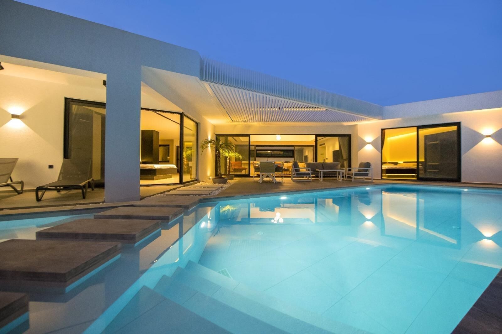 A modern pool area with a clear pool, lounge chairs, and a well-lit interior space.
