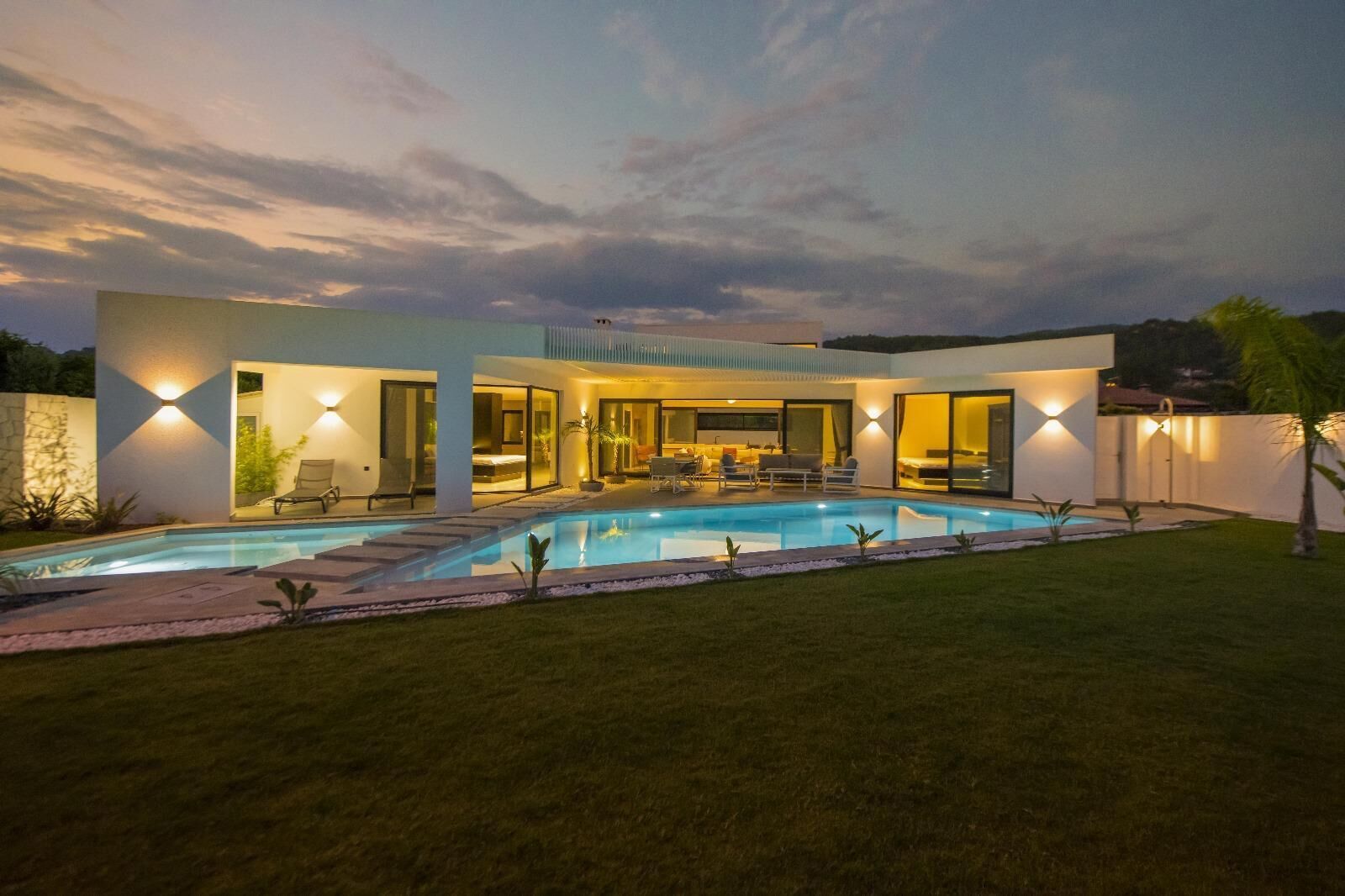 A modern house with a swimming pool, outdoor seating, and a well-lit patio area.
