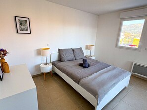 Ein Schlafzimmer mit einem Bett, zwei Nachttischen, einem Fenster und einem Bild an der Wand.