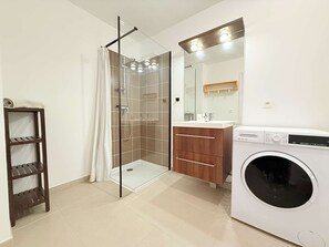 Ein modernes Badezimmer mit einer gläsernen Duschkabine, einem Holzbadezimmer-Möbel, einer Waschmaschine und einem Regal mit einem Handtuch.