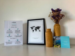 A framed world map, a welcome sign, a framed notice, a wooden bottle, and a brochure on a table. - Apartment with pool and parking - 4 guests (Le Lavandou)
