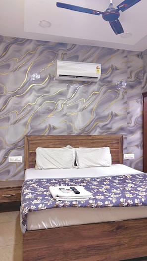 Una habitación de hotel con cama, ventilador de techo, aire acondicionado y una pared con diseño tipo mármol.