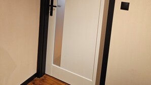 Una habitación con piso de madera, una puerta blanca con marco negro y un interruptor pequeño en la pared.