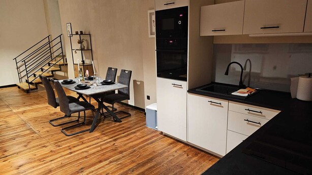 Una cocina compacta con comedor, suelo de madera y una escalera.