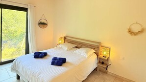 Quarto com uma cama grande, duas luminárias de cabeceira, uma janela com cortinas e uma planta na parede.