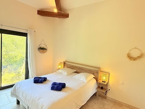 Ein Schlafzimmer mit einem großen Bett, zwei Nachttischlampen, einem Fenster mit Vorhängen und einer Wandpflanze.