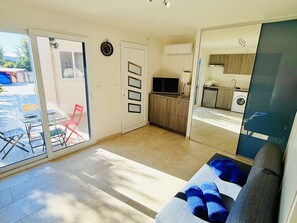 Uma sala de estar moderna com um sofá, uma televisão e uma porta de vidro deslizante que dá para um pátio.