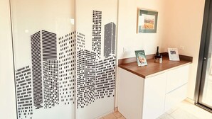 Uma mesa de recepção com uma obra de arte urbana na parede, um letreiro de boas-vindas emoldurado e uma garrafa no balcão.