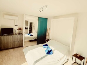 Quarto de hotel com cama, televisão, guarda-roupa e banheiro visível por uma porta aberta.
