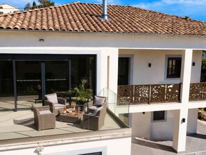 Ein modernes Haus mit Ziegeldach, einer überdachten Terrasse und Gartenmöbeln sowie einem Glasgeländer.