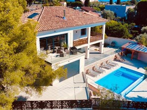 Ein modernes, zweistöckiges Haus mit Swimmingpool, Außenmöbeln und einer überdachten Terrasse.