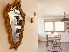 Ein Essbereich mit Tisch und Stühlen, einem großen, verzierten Spiegel und einem Fenster mit Jalousien.