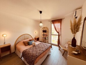 A bedroom with a bed, bedside lamps, a bookshelf, a window with curtains, and a mirror. - Apartment with AC, parking, near the sea (Le Lavandou)