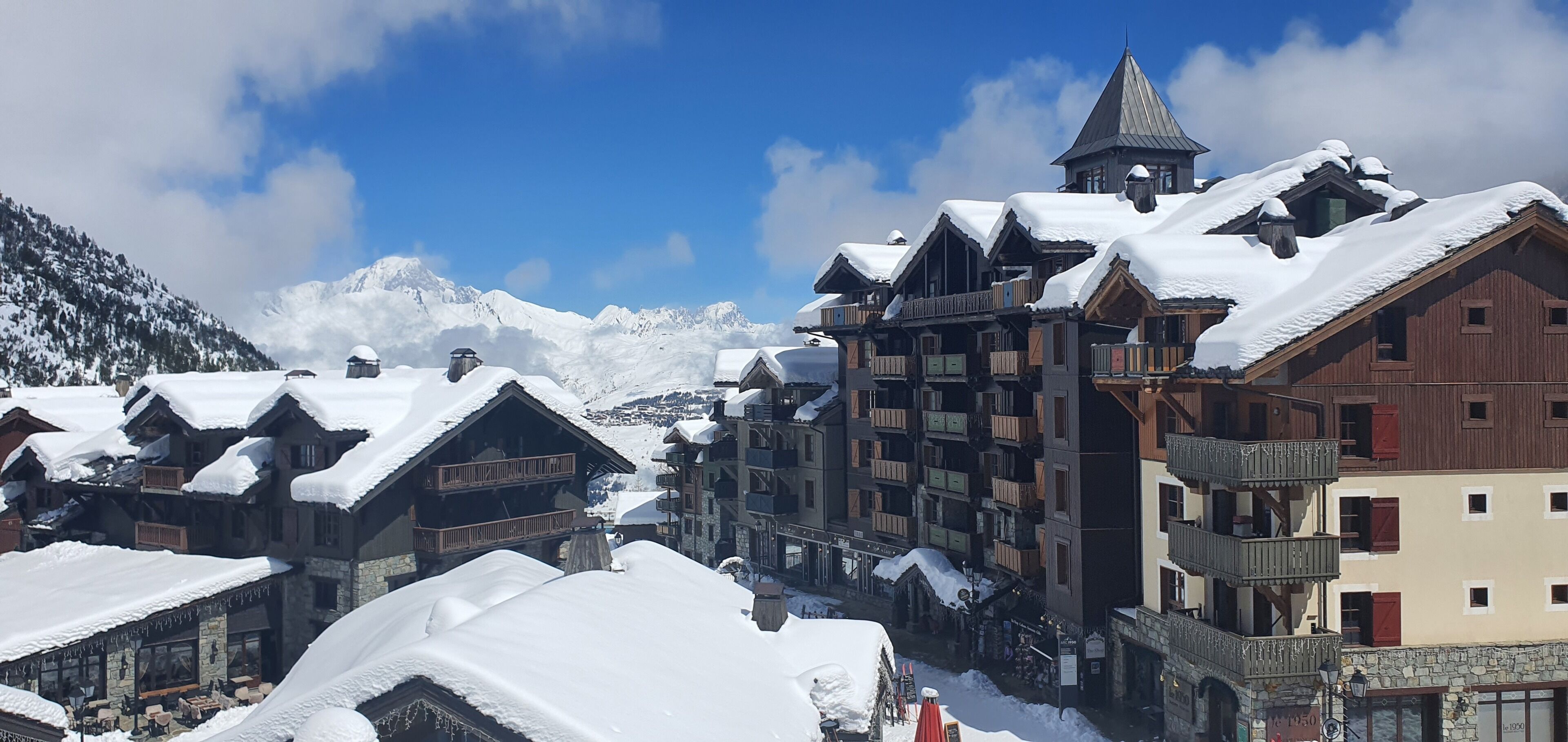A snow-covered village with traditional wooden buildings, a ski lift, and a mountain backdrop.