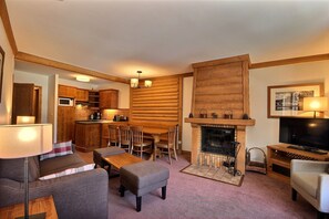A cozy living room with a fireplace, a television, and a dining area. - Coeur Arc 1950 — 80 m² duplex, 3 bedrooms, ski-in/ski-out, 5★ with pool (Bourg-Saint-Maurice)