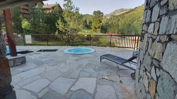 Une terrasse extérieure en pierre, avec une piscine, des chaises longues et un mur en pierre.