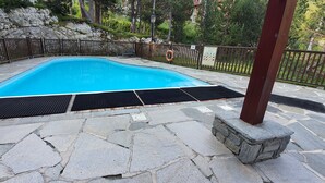 Une piscine dotée d’une plage en pierre, entourée d’une clôture en bois et d’un mur en pierre.