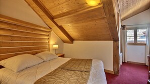 Une chambre avec un plafond en bois, un lit avec une literie blanche, une table de chevet et une fenêtre avec des rideaux.