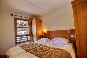 A bedroom with a bed, a window, a wooden wardrobe, and a wall-mounted light fixture. - Auberge Jérôme 614 — 80 m² duplex, 3 bedrooms, ski-in/ski-out, 5★ with a pool (Bourg-Saint-Maurice)