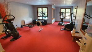 Une salle de sport équipée de divers appareils d’exercice, d’un distributeur d’eau et de grandes fenêtres laissant entrer la lumière naturelle.