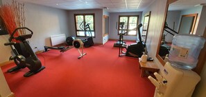A gym with various exercise equipment, a water dispenser, and large windows allowing natural light. - Coeur Arc 1950 — 80 m² duplex, 3 bedrooms, ski-in/ski-out, 5★ with pool (Bourg-Saint-Maurice)