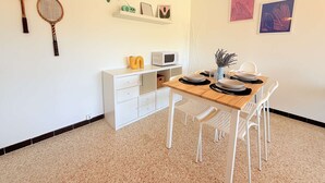 En matplats med ett träbord, vita stolar, ett vitt skåp och föremål som hänger på väggen, inklusive två tennisracketar, en radio och inramade konstverk.