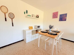 Ein Essbereich mit einem Holztisch, weißen Stühlen, einer weißen Kommode und an Wänden angebrachten Gegenständen, darunter zwei Tennisschläger, ein Radio und gerahmte Kunstwerke.