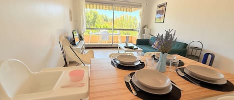 Un comedor con una mesa de madera dispuesta para cuatro, sillas blancas y vistas al exterior a través de un ventanal.