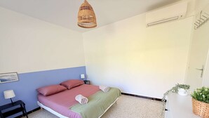 Ett sovrum med en säng, sängbord, en lampa, en hängande taklampa och en krukväxt.