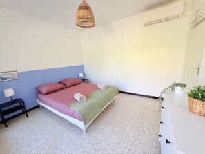 Ein Schlafzimmer mit einem Bett, Nachttischen, einer Lampe, einer Pendelleuchte und einer Zimmerpflanze.