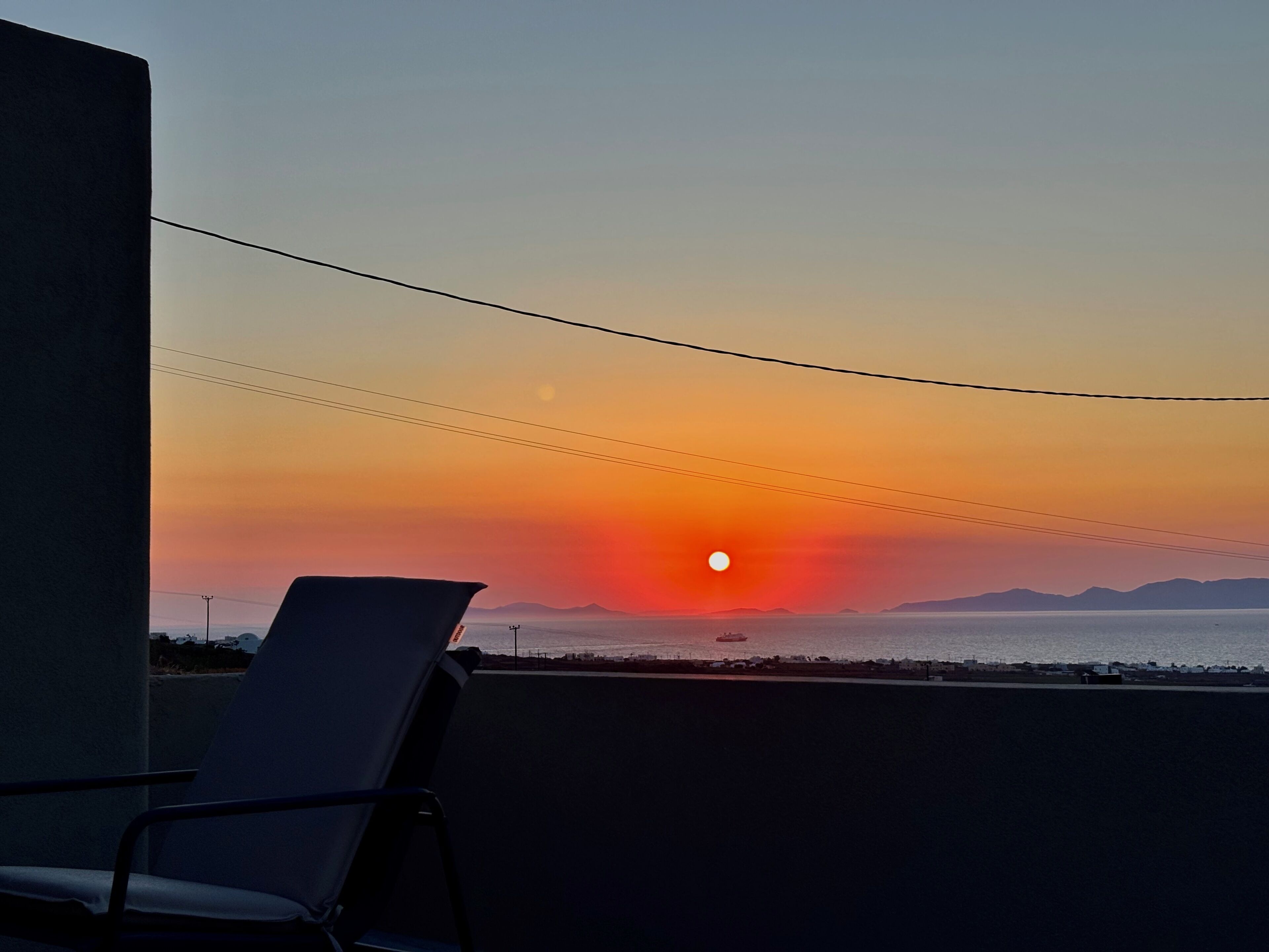 Una silla mirando al atardecer sobre el agua, con montañas a lo lejos.
