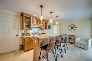 A kitchen with a central island, bar stools, wooden cabinets, and pendant lighting. - Casa Zoe — Sunset Canal Retreat in SE Cape Coral with huge heated pool and spa, kayaks, bikes, fishing poles, and dartboard (Cape Coral)