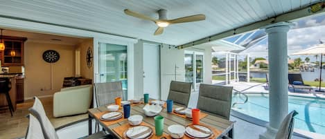 A covered outdoor dining area with a pool view, a ceiling fan, and a kitchen area with a dartboard.
