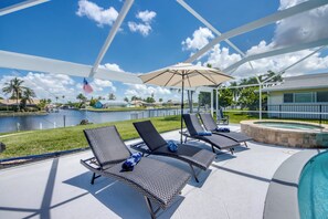 Ein Poolbereich mit Liegestühlen und einem Sonnenschirm mit Blick auf ein Gewässer und einen angelegten Garten.