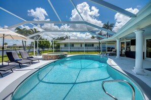 A swimming pool with lounge chairs and umbrellas, surrounded by a covered patio area. - Casa Zoe — Sunset Canal Retreat in SE Cape Coral with huge heated pool and spa, kayaks, bikes, fishing poles, and dartboard (Cape Coral)