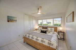 A bedroom with a bed, bedside tables, a ceiling fan, a window with a view, and a painting on the wall. - Casa Zoe — Sunset Canal Retreat in SE Cape Coral with huge heated pool and spa, kayaks, bikes, fishing poles, and dartboard (Cape Coral)