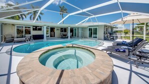 A pool area with a hot tub, lounge chairs, and umbrellas. - Casa Zoe — Sunset Canal Retreat in SE Cape Coral with huge heated pool and spa, bikes, fishing poles, and dartboard (Cape Coral)