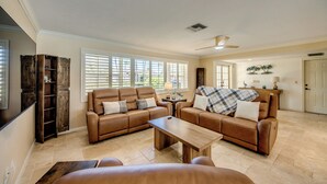 A spacious living room with a brown leather sofa set, a wooden coffee table, and a television mounted on the wall. - Casa Zoe — Sunset Canal Retreat in SE Cape Coral with huge heated pool and spa, bikes, fishing poles, and dartboard (Cape Coral)