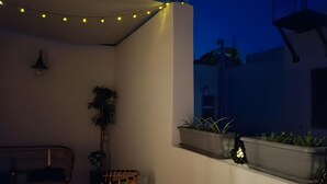 A balcony with string lights, a wicker chair, potted plants, and a wall-mounted light fixture. - Casa Autentica 1933 Apartment with Private Balcony (Kos)